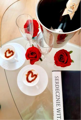 a glass table with two wine glasses and roses at Hotel Bursztyn in Kalisz