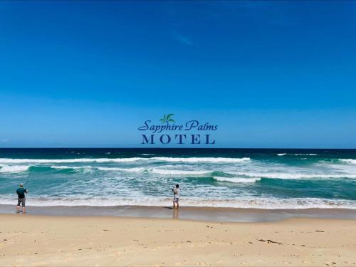 dos personas de pie en una playa con el océano en Sapphire Palms Motel, en The Entrance
