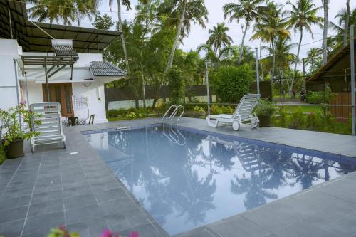 einen Pool mit zwei Liegestühlen und Palmen in der Unterkunft Waves and Shores Beach Villa in Mararikulam