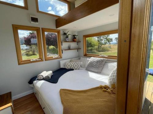 a bedroom with a large white bed with windows at 'Bertie' Tiny House on a Lake in a Vineyard in Hall