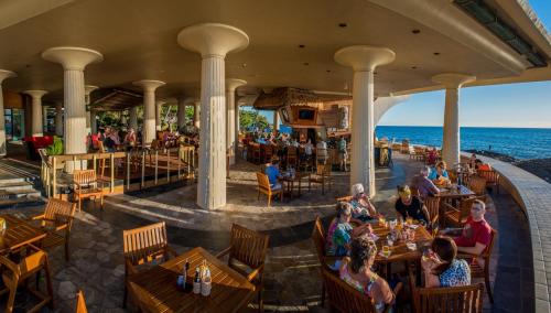 people sitting at tables in a restaurant next to the ocean at Royal Kona Resort in Kailua-Kona