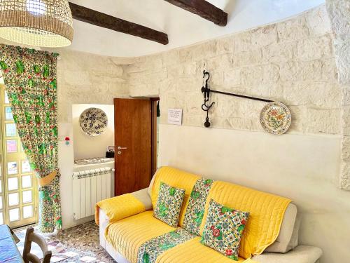 un soggiorno con divano giallo e parete in pietra di Trulli Fenice a Martina Franca