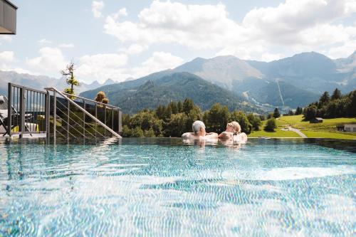 two people in a swimming pool with mountains in the background at Alpine Resort Goies Superior in Ladis