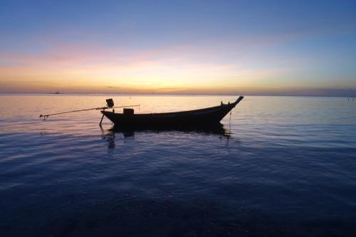 a boat sitting in the water at sunset at The Rendezvous Hostel in Haad Rin