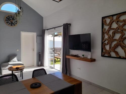 a living room with a table and a tv on a wall at Bungalow La Palmera - 2 bedroom - PLAYA ROCA residence sea front access - Pool View - Free AC - Wifi in Costa Teguise