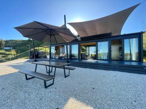 uma casa com uma mesa de piquenique e um guarda-chuva em Waitomo Retreat em Hangatiki