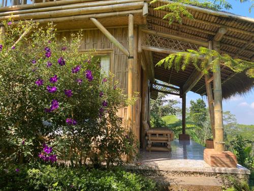 un porche de una casa de madera con flores púrpuras en Lembah Cinta Mayungan, en Baturiti