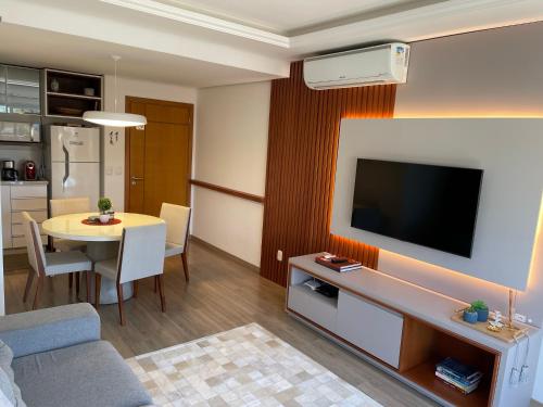 un salon avec une télévision et une table avec des chaises dans l'établissement Excelente apartamento em Gramado/RS no Condomínio Casa de Pedra, à Gramado