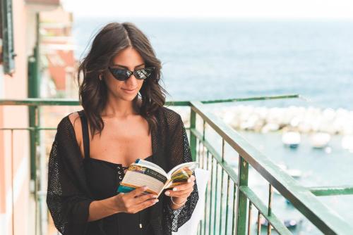 a woman reading a book on a balcony at EC Luxury Rooms in Riomaggiore