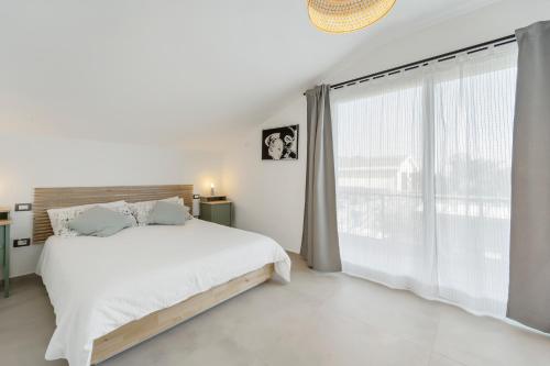 a white bedroom with a bed and a large window at La Pimpinella in Su Forti