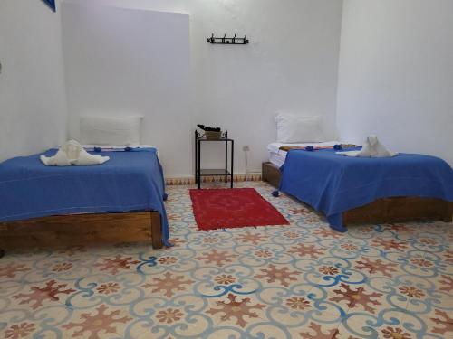 a room with two beds and a red rug at Riad AYLAL in Essaouira