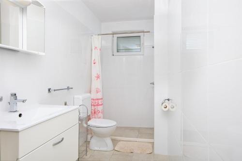 a white bathroom with a toilet and a shower at Apartments Mrak in Punat