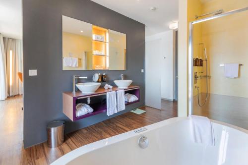 a bathroom with a tub and two sinks and a mirror at Parkhotel Brenscino Brissago in Brissago
