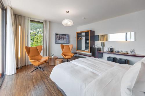 a bedroom with a bed and two chairs and a kitchen at Parkhotel Brenscino Brissago in Brissago