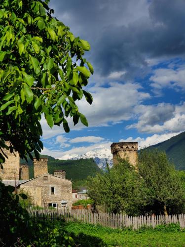 an old building with a fence and mountains in the background at Ailama Guesthouse in Mestia