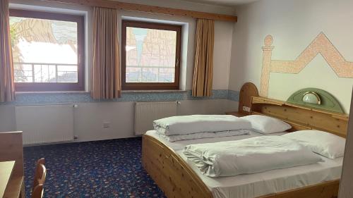 a bedroom with two beds and a table and two windows at Hotel Saxl in Campo di Trens