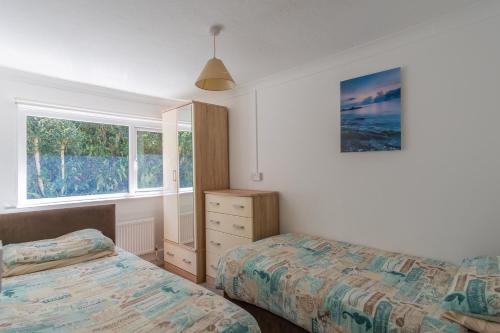 1 Schlafzimmer mit 2 Betten, einer Kommode und 2 Fenstern in der Unterkunft Deluxe Kipling Villa with Sea Views in Bideford