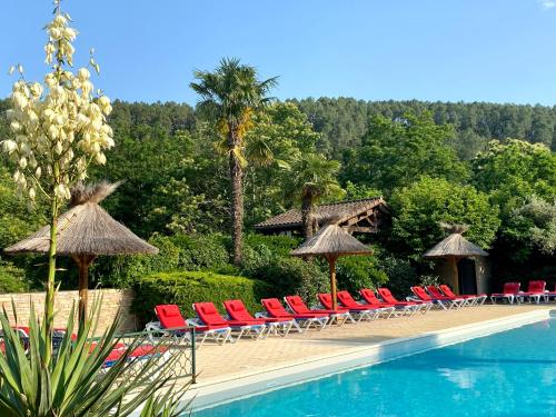 a swimming pool with red chairs and umbrellas at Hameau du Prat in Ribes