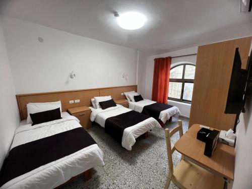 a room with three beds and a desk and a television at William's Guest House in Jerusalem