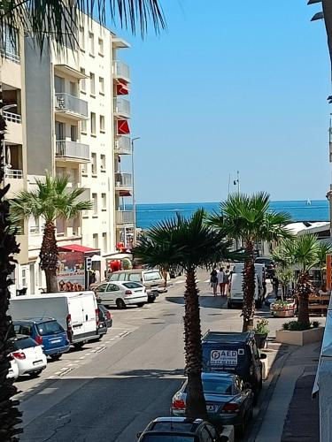 une rue de la ville avec des palmiers et l'océan dans l'établissement Studio Palavas proche plages et centre - terrasse - Clim & Parking, à Palavas-les-Flots