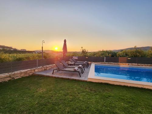 a swimming pool with chairs and a sunset in the background at Villa Dionisia with private pool in Roumelí