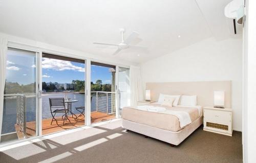 a white bedroom with a bed and a balcony at Driftwood Apartment 6, Noosaville in Noosaville