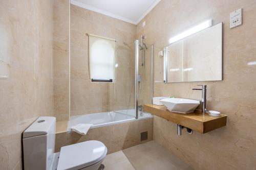 a bathroom with a toilet and a sink and a tub at Hotel Residencial Salema in Salema
