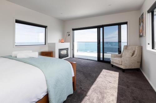 Oakura Beach Front Apartments في Oakura: غرفة نوم بسرير وكرسي ونوافذ