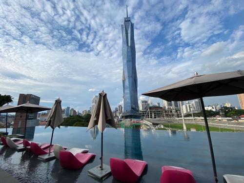 a pool with chairs and umbrellas in front of a city at ASTRA at Opus Residences Kuala Lumpur in Kuala Lumpur