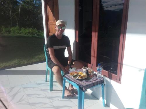 Un uomo seduto su una sedia con un piatto di cibo su un tavolo di Rice field guest house a Kelimutu