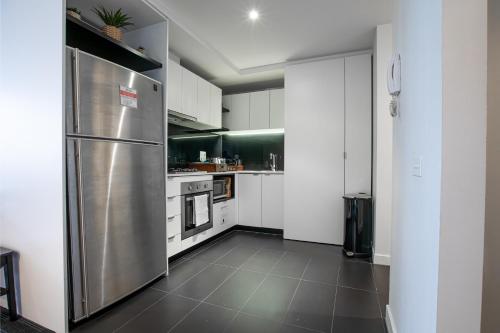 a kitchen with a stainless steel refrigerator and white cabinets at ‘Sunrise on Aura’ Apartment with stunning views. in Melbourne