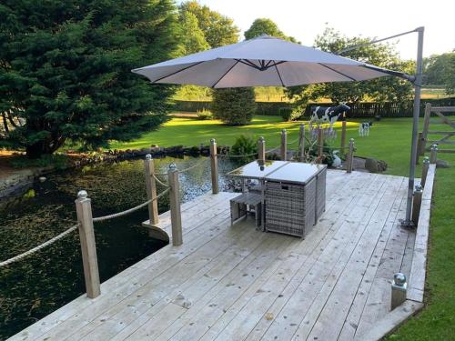 a wooden deck with a table and an umbrella at The Coo Shed in Balfron