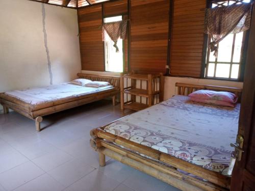 two beds in a room with wooden walls and windows at Lorenso Cottage in Manado