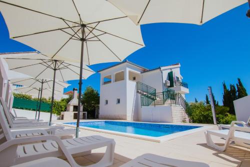 a villa with a swimming pool and umbrellas at Apartments M in Seget Vranjica