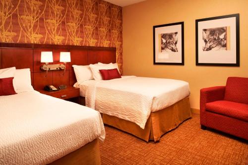 a hotel room with two beds and a red chair at Courtyard Toledo Airport Holland in Holland