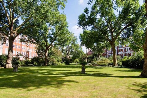 um parque com árvores e um edifício ao fundo em Lovely 2-beds flat in the heart of Knightsbridge em Londres