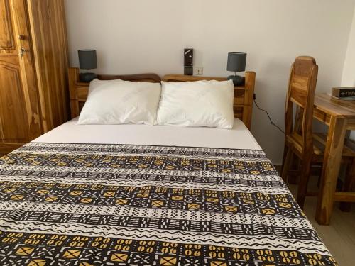 a bed in a room with a table and a bedspread at pavillon « lilas » à dagué-togo in Dagé