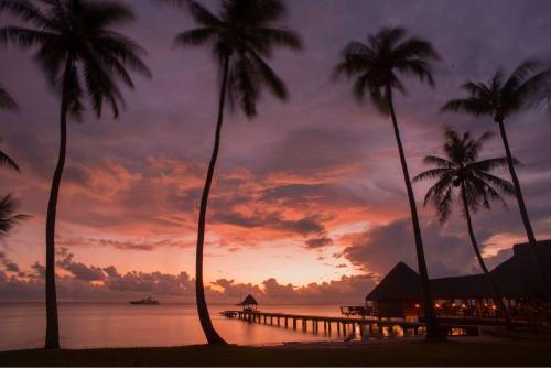 a sunset on a beach with palm trees and a pier at Hotel Kia Ora Resort & Spa in Avatoru