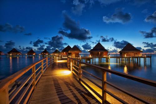 a pier with overwater bungalows on the water at night at Hotel Kia Ora Resort & Spa in Avatoru