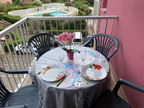 une table avec deux assiettes et un vase de fleurs sur le balcon dans l'établissement "Le Pharo" 17 Impasse du globe Appartement, au Cap d'Agde