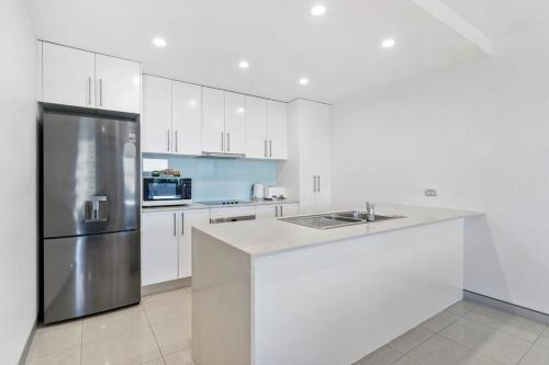 a kitchen with white cabinets and a stainless steel refrigerator at Redvue Holiday Apartments in Redcliffe