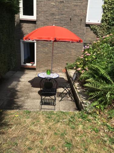 a table and chairs with a red umbrella at Aangename en zeer rustig gelegen vakantiewoning in Westdorpe