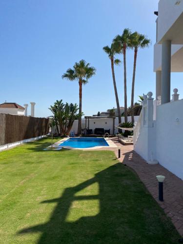 un patio trasero con piscina y palmeras en Villa Las Americas en Sotogrande