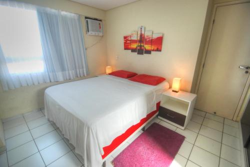 1 dormitorio con 1 cama blanca y 2 almohadas rojas en Apartamentos Verano, en Natal