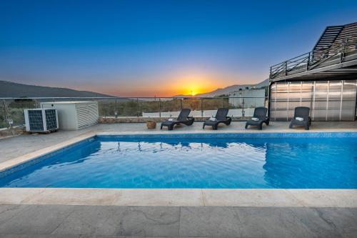 a pool with chairs and the sunset in the background at צימר בכפר - סוויטות ובקתות קסומות עם בריכה מחוממת ונוף מהמם in Rama