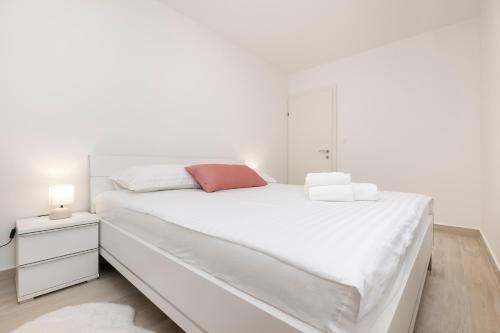 a white bedroom with a large white bed and a night stand at Apartments Tony in Mali Lošinj