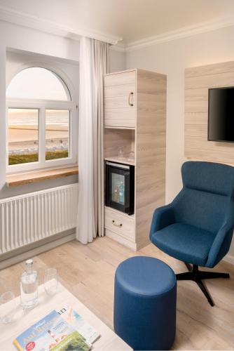 a living room with a blue chair and a tv at Strandhotel Gerken in Wangerooge