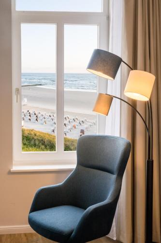 a chair next to a lamp and a window with the beach at Strandhotel Gerken in Wangerooge