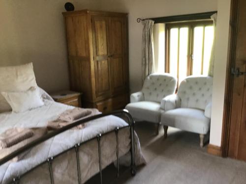 a bedroom with a bed and two chairs and a window at Owletts Barn B&B in Bodmin