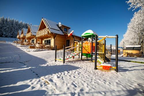 a playground in the snow in front of a building at Domki Osada Zieleniec in Duszniki Zdrój